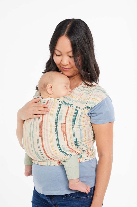 Mama tuli niemowlaka w Chuście elastycznej Tula Geode w pasy w rożnych kolorach z tkaniny Tencel