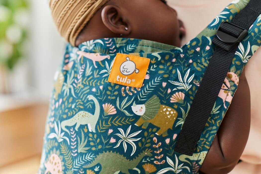 Zbliżenie na wzór nosidełka Tula Free-to-Grow Land Before Tula - dinozaury w różnych odcieniach zieleni ibujna roslinność na butalkowo-zielonym tle.