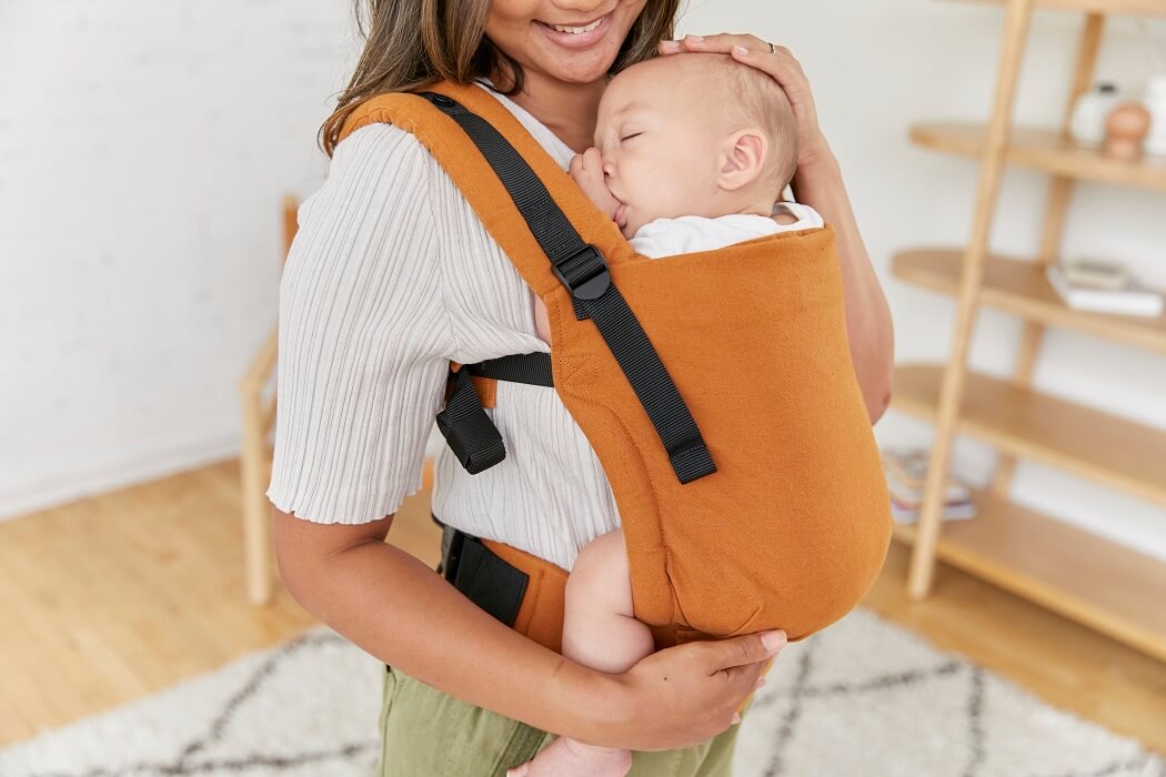 Mama nosi śpiące dziecko w ergonomicznym nosidełku Free-to-Grow Hemp Amber.
