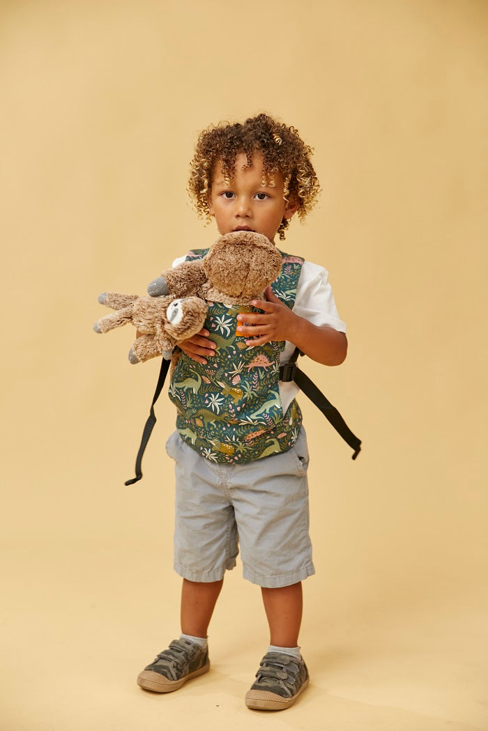 A boy carrying his toy in Tula Mini Doll Carrier in fun dinosaur print