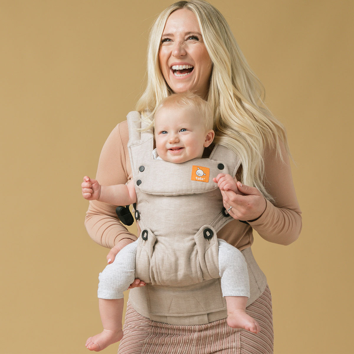 Uśmiechnięta mama z dzieckiem w nosidełku Tula Explore w pozycji przodem do świata