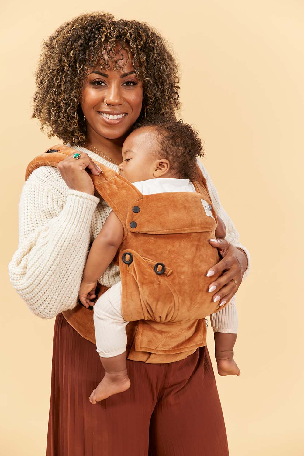 Uśmiechnięta mama z dzieckiem w nosidełku Tula Explore Velour Caramel
