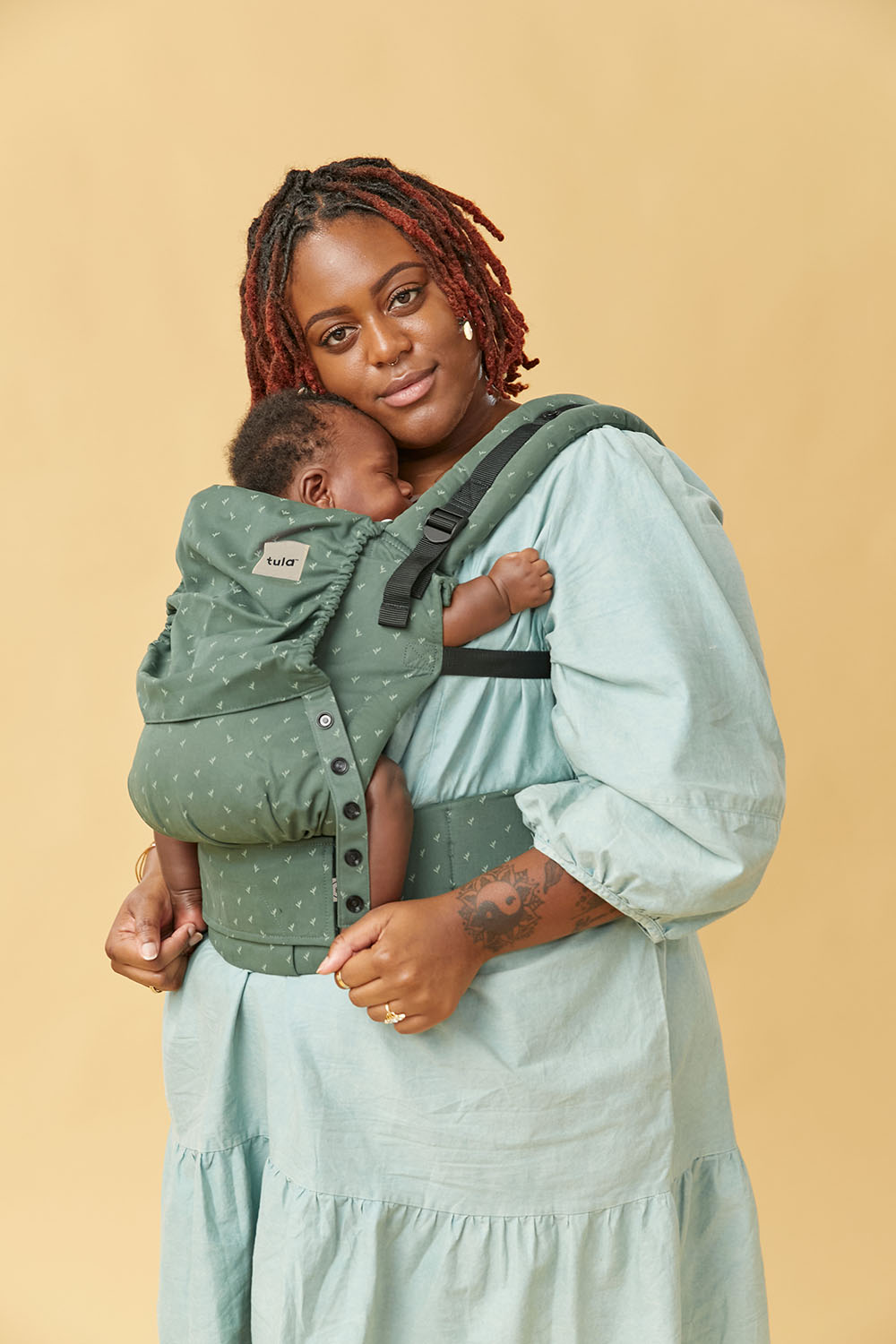 Mama nosi malutkie dziecko w nosidełku Tula Free-to-Grow w ergonomicznej pozycji przodem do rodzica.