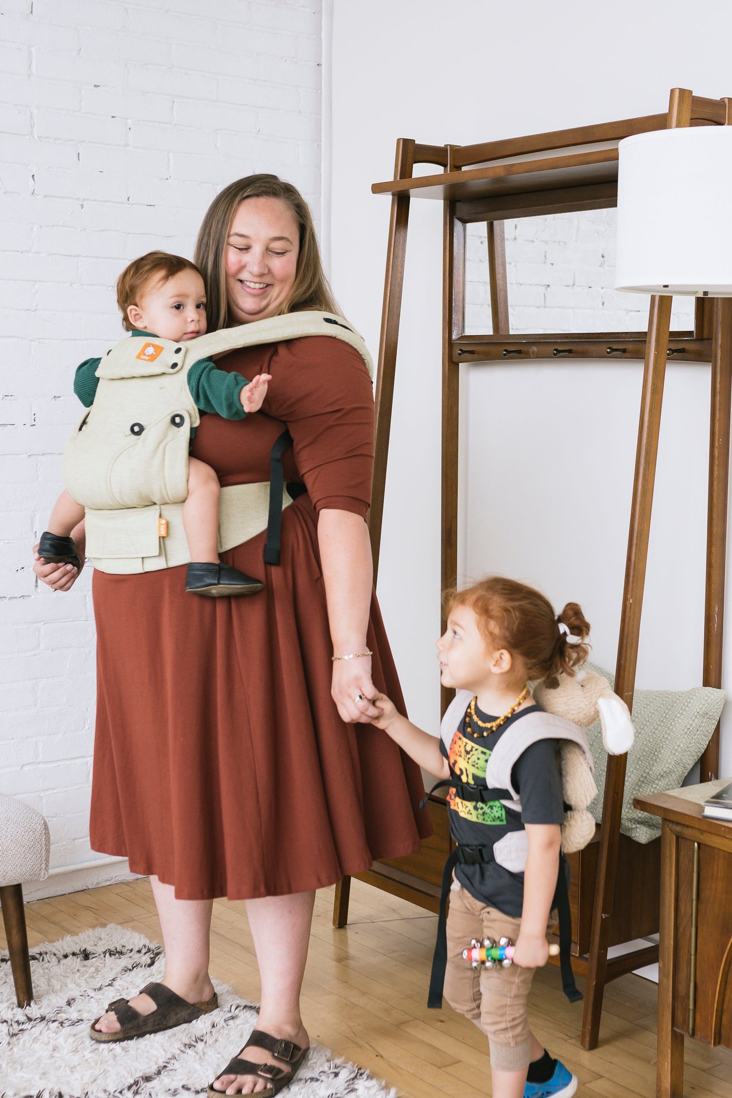 Uśmiechnięta mama w towarzystwie starszego dziecka nosi niemowlaka w nosidełku Tula Linen Explore Moss z mieszanki lnu i bawełny