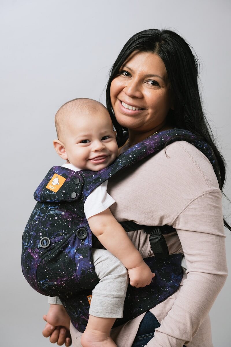 Uśmiechnięta mama nosi radosne niemowlę w nosidełku Tula Explore Andromeda
