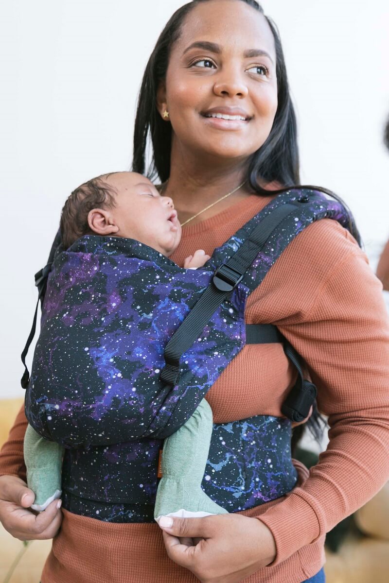 Mama nosi śpiącego noworodka w nosidełku Tula Free-to-Grow w pozycji przodem do rodzica.