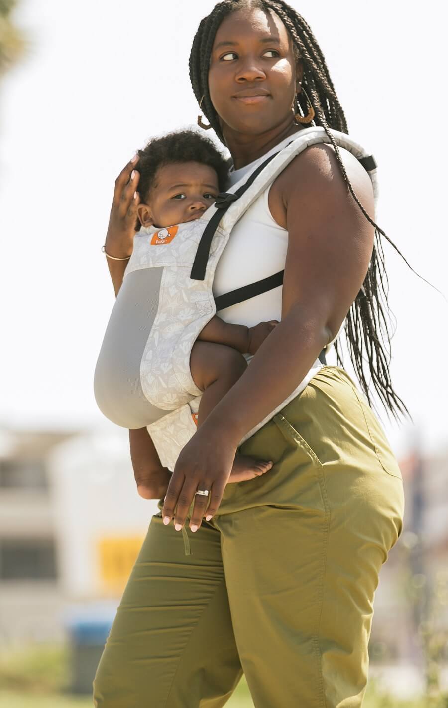 Mama nosi dziecko w ergonomicznym nosidełku Tula Free-to-Grow w pozycji przodem do rodzica.