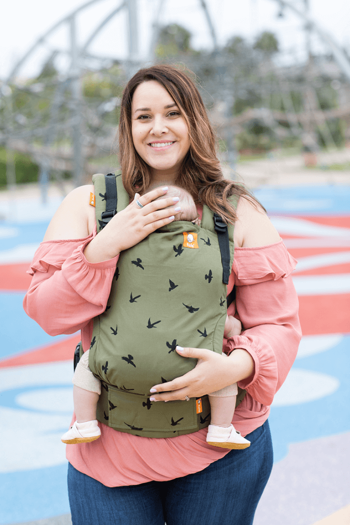 Mama nosi niemowlę w nosidełku Tula Free-to-Grow w pozycji przodem do rodzica.