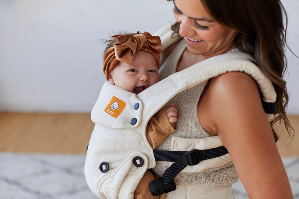 Roześmiane niemowlę noszone przez mamaę w nosidełku Tula Linen Explore Dove