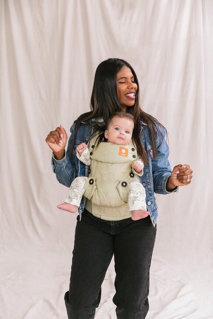 Roztańczona mama nosi dziecko w nosidełku Tula Explore Moss z mieszanki lnu i bawełny w pozycji przodem do świata