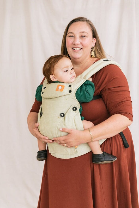 Uśmiechnięta mama nosi dziecko w nosidełku Tula Linen Explore Moss z mieszanki lnu i bawełny