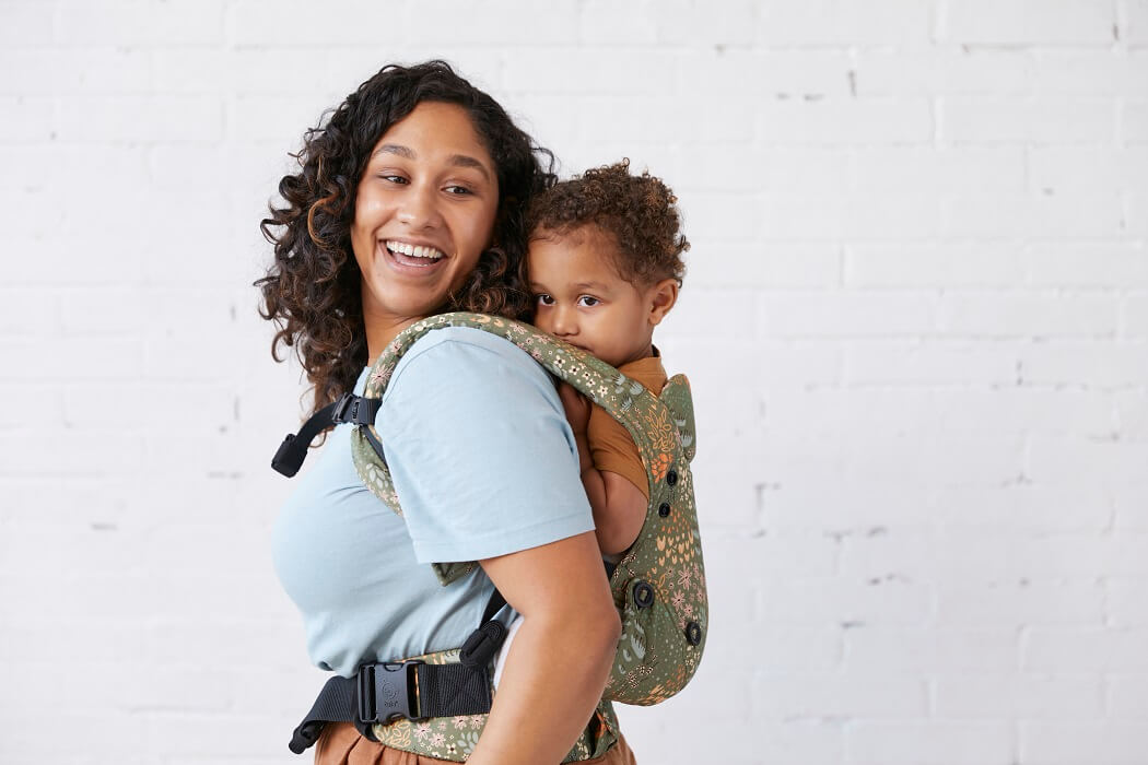 Uśmiechnięta mama nosi dziecko w nosidełku Tula Explore w pozycji na plecach