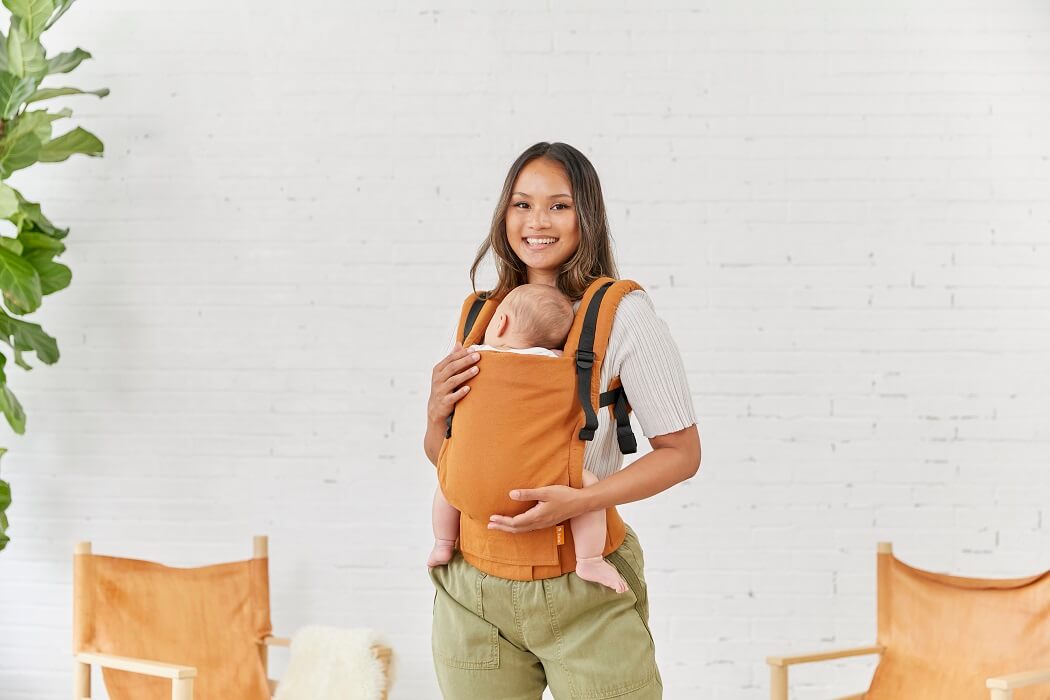 Uśmiechnięta mama nosi dziecko w nosidełku ergonomicznym dla niemowlaka w pozycji z przodu.