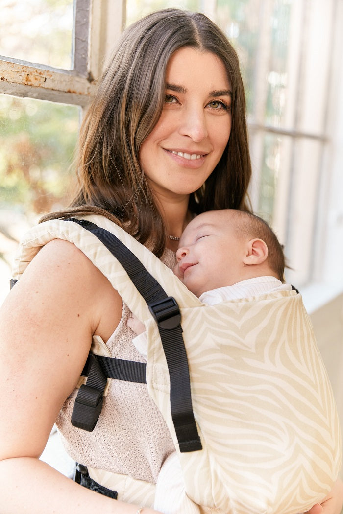 Mama nosi śpiace dziecko w nosidełku Tual free-to-Grow w ergonomicznej pozycji przodem do rodzica.