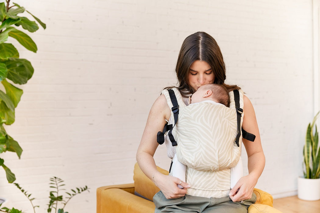 Mama nosi śpiące dziecko w nosidełku Tual free-to-Grow w ergonomicznej pozycji przodem do rodzica.