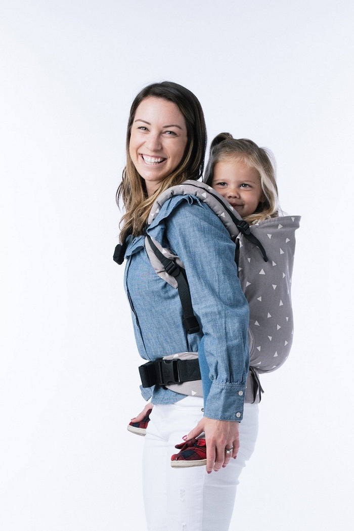 Uśmiechnięta mama nosi dzieko w wygodnej pozycji na plecach w nosidełku Tula Toddler