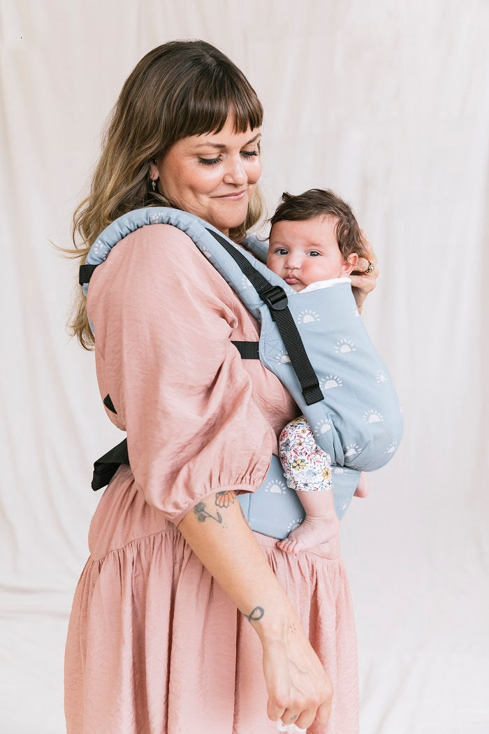 Uśmiechnięta mama nosi dziecko w ergonomicznym nosidełku Tula Free-to-Grow 