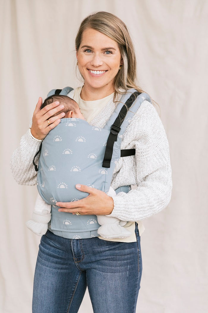 Uśmiechnięta mama nosi dziecko w ergonomicznym nosidełku Tula Free-to-Grow