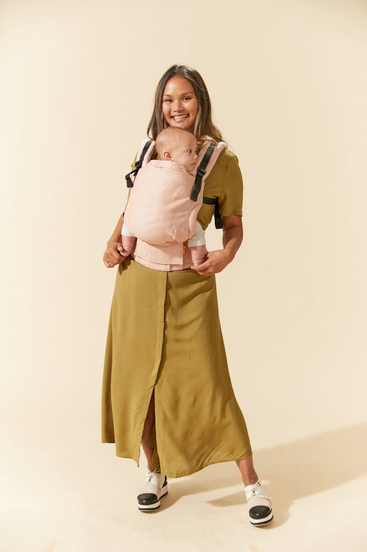 Uśmiechnięta mama nosi swoje dziecko w ergonomicznym nosidełku Free-to-Grow Linen Sunset marki Tula