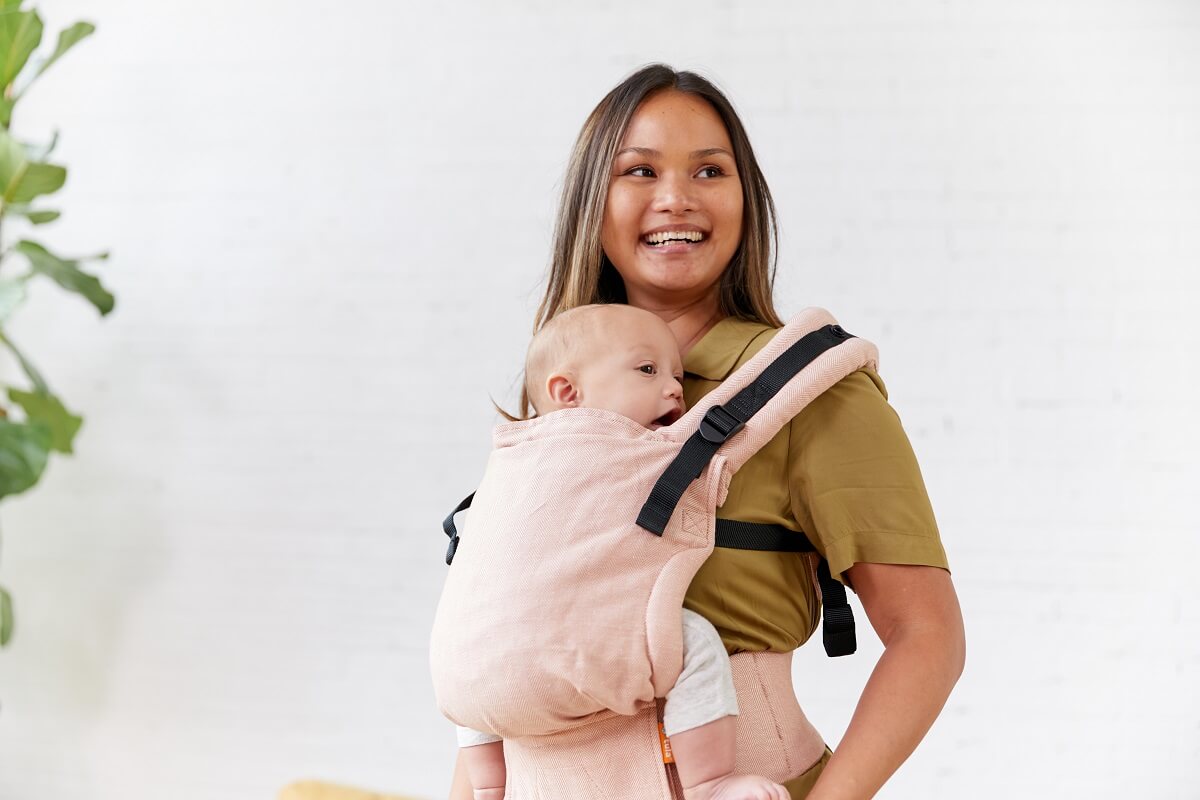 Mama nosi swoje dziecko w ergonomicznym nosidełku Free-to-Grow Linen Sunset marki Tula