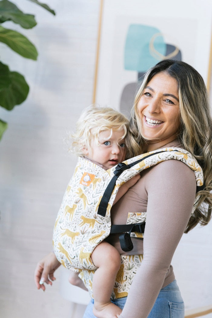 Uśmiechnięta mama nosi dziecko w ergonomicznej pozycji w nosidełku Tula Free-to-Grow Prowl