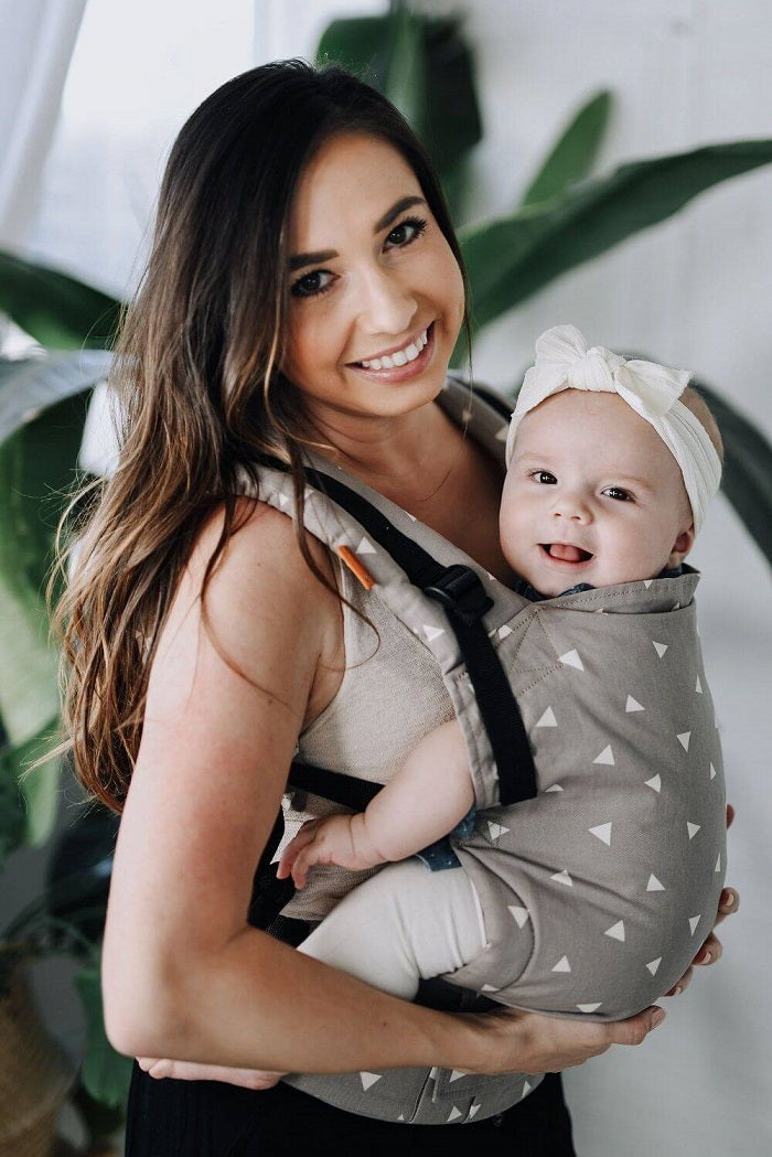 Uśmiechnięta mama nosi dziecko w nosidełku Tula Free-to-Grow dla noworodków