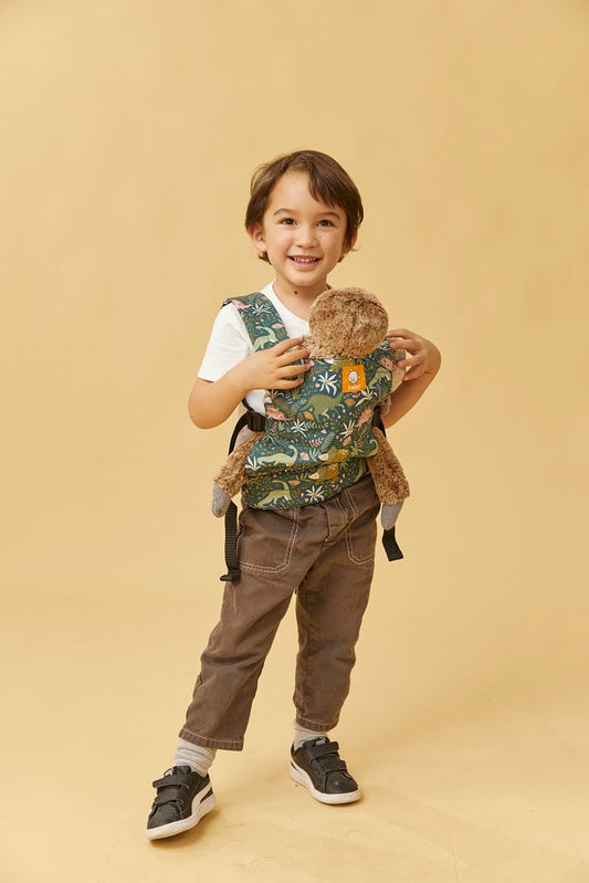 A boy carrying his toy in Tula Mini Doll Carrier in fun dinosaur print