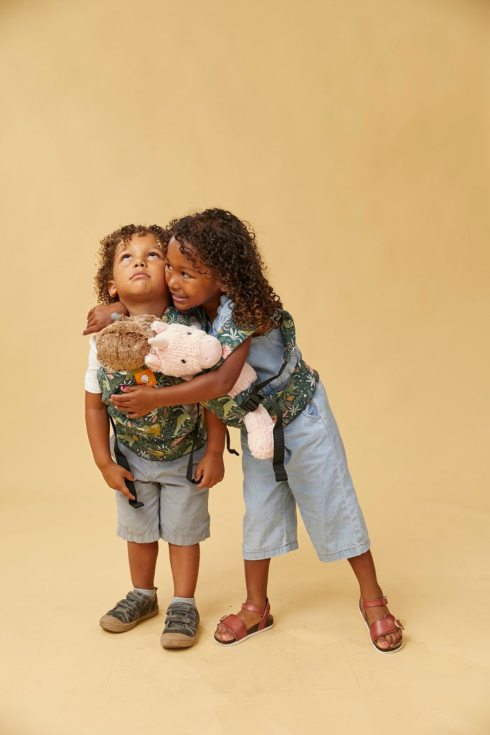 A girl hugging a boy carrying his toy in Tula Mini Doll Carrier in fun dinosaur print